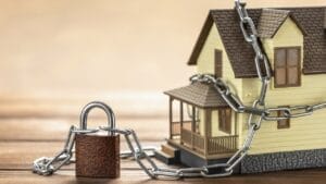 Don’t Get Fooled: Safeguard Your Home Title from Scams 1 Don’t Get Fooled: Safeguard Your Home Title from Scams - House tied with a chain and a closed lock ss2049458297