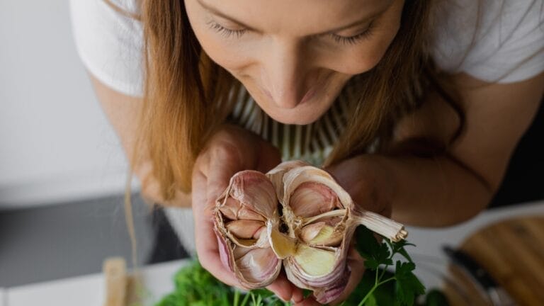 Improve Your Skin Naturally by Adding Garlic to Your Skincare Routine 6 Improve Your Skin Naturally by Adding Garlic to Your Skincare Routine - woman smiling holding garlic ss2170612481