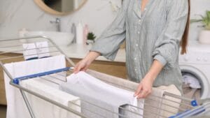 13 Clever Ways to Dry Clothes Indoors Without a Dryer 1 13 Clever Ways to Dry Clothes Indoors Without a Dryer - woman hanging clean laundry on drying rack ss1924381058