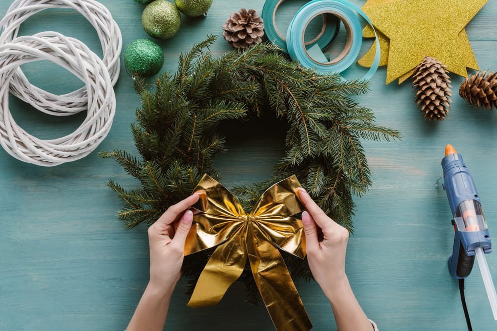 25 Unique Christmas Wreaths to Elevate Your Holiday Decor 5 25 Unique Christmas Wreaths to Elevate Your Holiday Decor - woman putting golden bow on handmade pine tree wreath dp221722562 dnoh