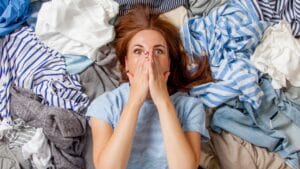 Don’t Toss These 16 Things When Decluttering—You Might Regret It Later 1 Don’t Toss These 16 Things When Decluttering—You Might Regret It Later - shocked woman lying down on clutter clothes dp404903738 dnoh